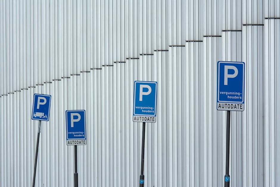 Four blue parking permit signs with white text and symbols are mounted on metal posts in front of a large, vertically ribbed metal wall. The signs indicate parking restrictions with the letter 'P' and include wording in Dutch, such as 'vergunning-houders' and 'AUTODATE.' The signs are arranged in a descending diagonal line from left to right, with the background wall reflecting natural light, creating a modern, industrial appearance. Although the image is focused on parking signage, it subtly relates to house removals and relocation services by highlighting parking permit management which is important for home relocation logistics, especially in urban areas like Ravenscourt Park. The signage and metallic environment contribute to a professional, neutral setting often associated with urban moving operations.